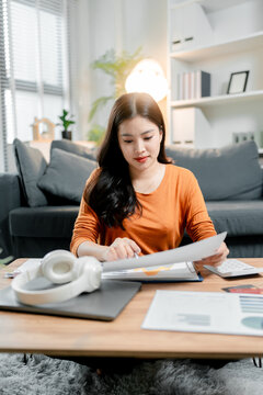 Young asian woman working from home, organizing business documents and financial reports, managing personal finances and budget in a modern living room