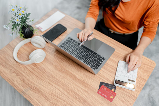 Person managing personal finances and online banking, calculating expenses and budgeting with a laptop, calculator, and credit cards on a home office table