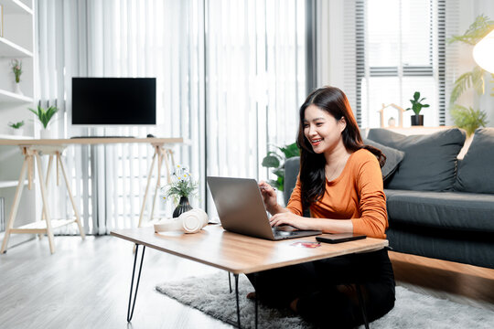 Young asian woman confidently working from home, smiling while typing on laptop keyboard, conducting online meeting or remote work in comfortable living room setting