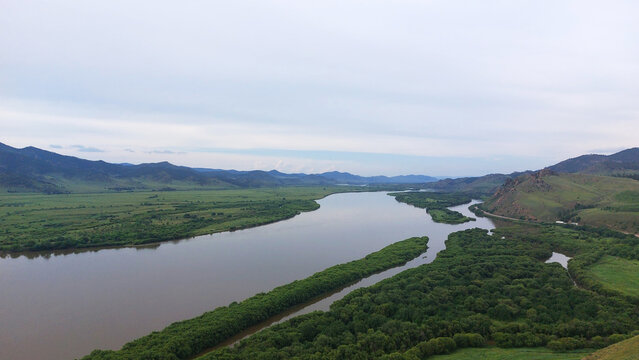 Winding Selenga River flowing through lush green valleys and forested islands in Buryatia, Siberia, with rolling hills under an overcast sky