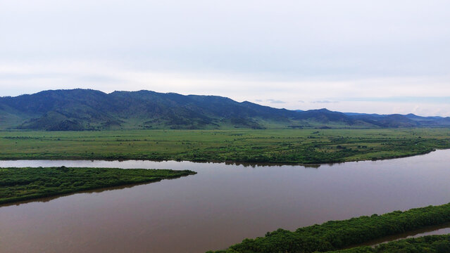 Winding Selenga River flowing through lush green valleys and forested islands in Buryatia, Siberia, with rolling hills under an overcast sky