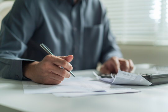 Close-up of office worker holding pen writing on financial document and checking bills at desk.