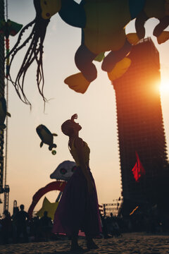 young woman walking on sand beach at colorful kite toys festival during summer sunset, girl enjoying freedom and joy at outdoor event by sea