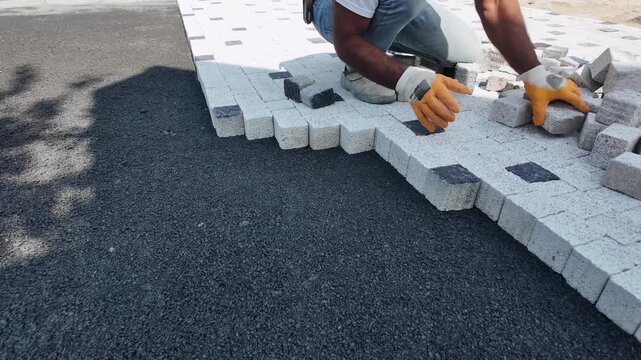 ISTANBUL, TURKEY - AUGUST 11, 2026: Close up of construction worker hands laying interlocking concrete paving blocks on sidewalk pavement during urban infrastructure and road renovation work