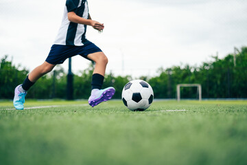 Fototapeta premium Kid boy leg kicking soccer ball on green grass field action. conceptual metaphor for youth sports training team competition fitness health wellness and active lifestyle