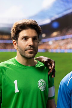 Goalkeeper in a green jersey and captain armband stands shoulder to shoulder with teammates in the pre-match national anthem ceremony ahead of kickoff.