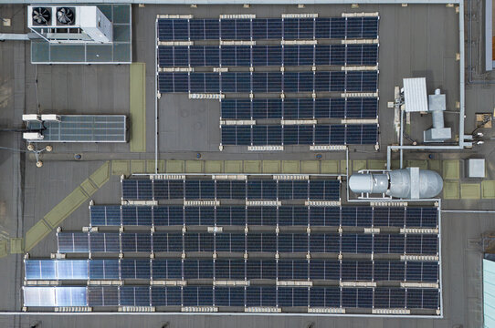 Aerial top-down view of solar panel arrays and HVAC equipment on flat industrial rooftop, commercial renewable energy and building infrastructure concept.