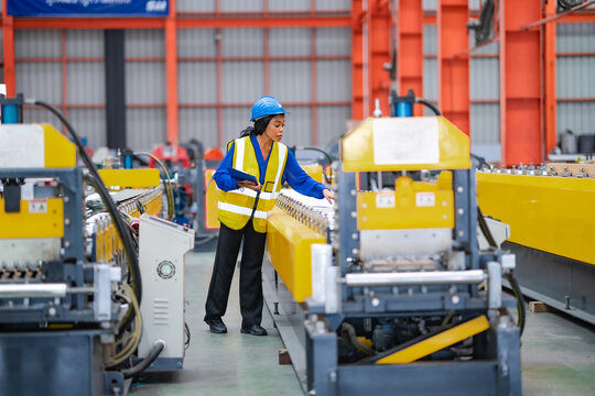 Female engineer checks production equipment by hand while holding clipboard on factory floor, industrial machinery inspection, manufacturing process, quality control.