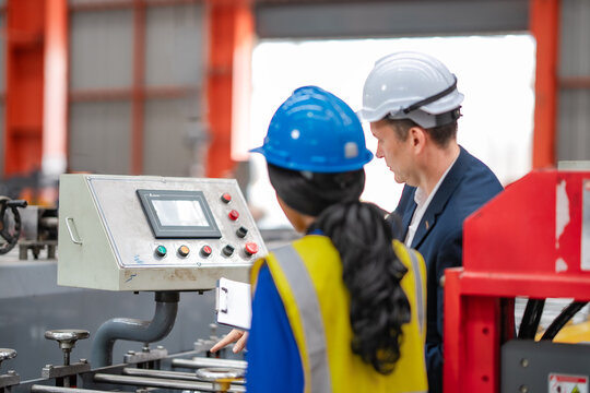 Factory manager and female engineer check machine control panel together, reviewing industrial equipment, production process, manufacturing operation, teamwork.