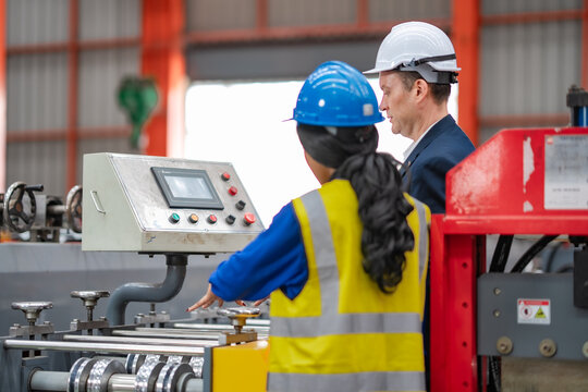Female engineer and factory manager monitor machine control panel and production equipment, industrial manufacturing, operation checking, teamwork, workplace safety.