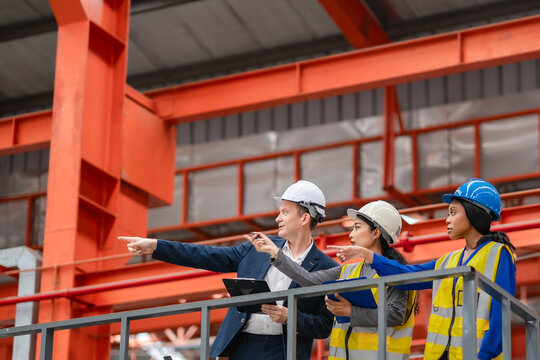 Factory manager and two female engineers point toward production area during factory inspection, industrial teamwork, manufacturing planning, quality control.