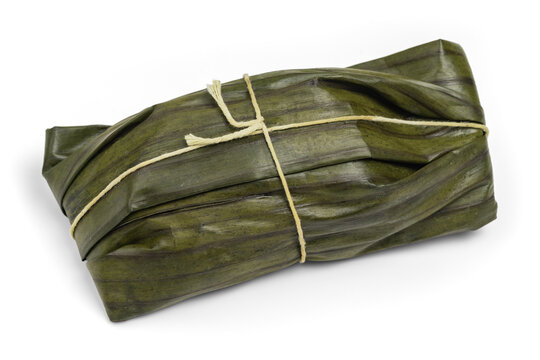 Traditional tamale wrapped in green leaves and tied with string, isolated on a white background. Typical Latin American steamed food.