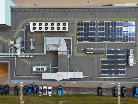 Aerial top-down view of commercial rooftop with solar panels and HVAC cooling units beside parking lot, building energy infrastructure and sustainability concept.