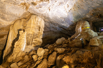 Wide view of large lit stalactites and stalagmites inside a spacious underground limestone cave chamber © wannasak