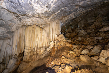 Large curtain stalactite drapery and rocky stone slope inside a vast natural limestone cave © wannasak