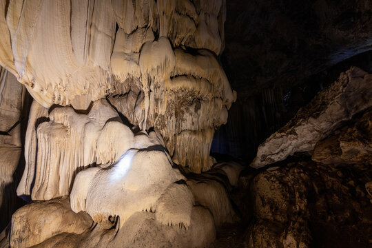 Detailed illuminated flowstone and stalactites inside a dark limestone cave chamber