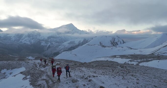 Annapurna Circuit, Manang region, Nepal, drone gliding shot across a line of trekkers hiking up a snow covered mountain slope during early morning light on the route to Thorong La Pass.