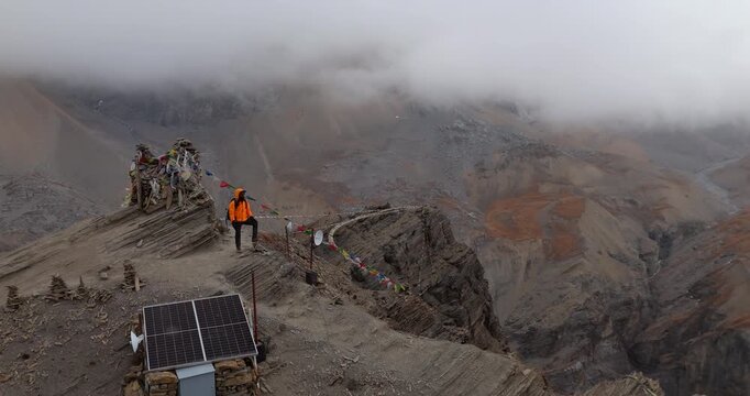 Annapurna Circuit, Manang region, Nepal, drone pull out shot of a male trekker standing at High Camp View Point beside stone cairns and prayer flags on the route to Thorong La.