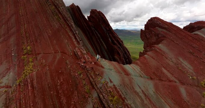 Travel couple stands on iconic Pallay Punchu rainbow mountain. Aerial reveal