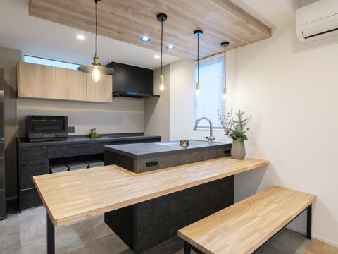 Modern Japandi kitchen and dining room interior design. Luxury home layout featuring island sink, integrated wooden table, bench and stylish pendant lights in a newly built house.