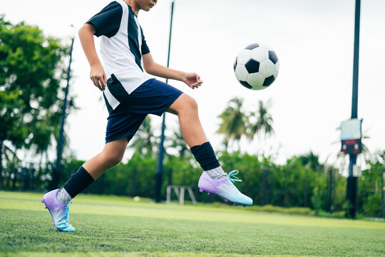 Kid boy leg kicking soccer ball on green grass field action. conceptual metaphor for youth sports training team competition fitness health wellness and active lifestyle