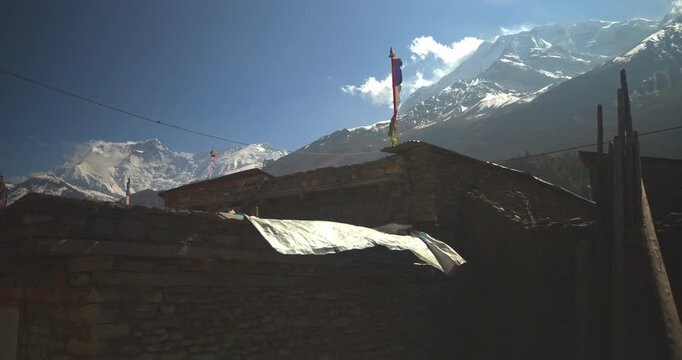 Annapurna Circuit, Manang village, Nepal, traditional stone houses with prayer flags set against snow-capped Annapurna mountain peaks.