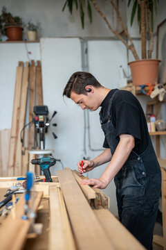 Thoughtful craftsman working with wooden parts for old window frame marking details with pencil, working process in restoration workshop, man woodworker preparing wood elements for renovation.