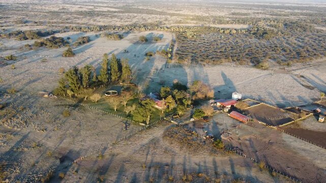 Sunrise aerial view of frozen rural fields and ranch infrastructure illuminated by warm morning sunlight in Argentina.