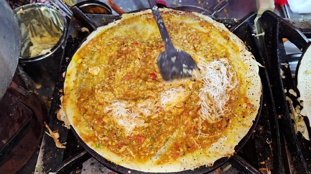 Close up of a street food vendor mixing grated cheese with spiced potato masala on a crispy dosa over a hot tawa while preparing a South Indian specialty at a food stall