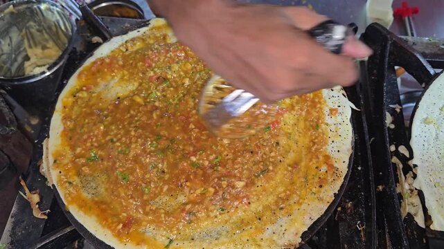Close up of a street vendor mashing and spreading spicy potato masala across a crispy dosa on a hot tawa while preparing a popular South Indian dish at an Indian food stall
