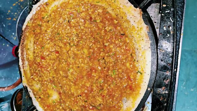 Close up of a street vendor grating fresh cheese over a spicy masala dosa on a hot tawa while preparing a crispy South Indian specialty at an Indian food stall.