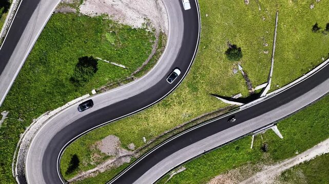 Aerial view of the winding mountain road at Passo Fedaia with cars driving through the green alpine landscape in Rocca Pietore, Veneto, Italy.