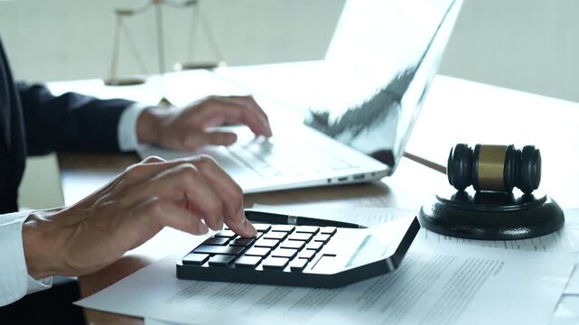 Lawyer working on a laptop at a desk with a gavel, scales of justice, documents and calculator, representing legal services, business law and professional consultation.	