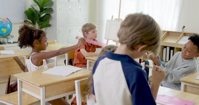 Elementary pupil group shares cheerful peer interaction at wooden desks, children exchange high five during back to school teamwork activity, building friendship, confidence, class participation