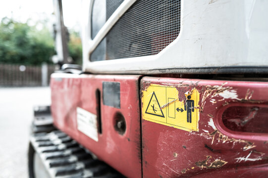 Shallow focus of yellow warning stickers attached to the read chassis of a mechanical excavator and digger, near the engine bay. Seen on a housing development site.