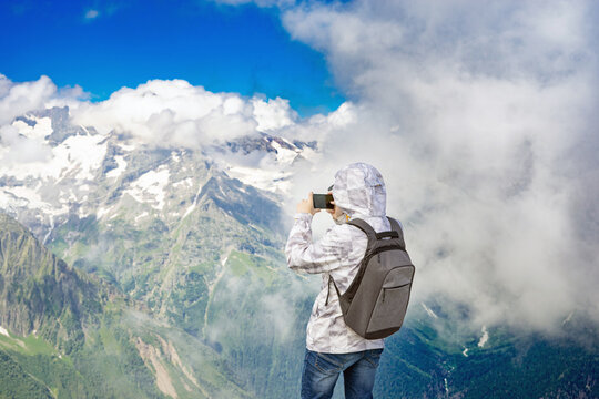 Young guy hiker looks out over spectacular Caucasian mountains with glaciers