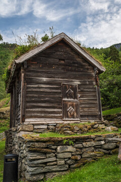 Vertical view of an old timber stabbur with a green grass turf roof resting on a dry stone wall at the historic Otternes Bygdetun farmstead in Aurland, Norway.