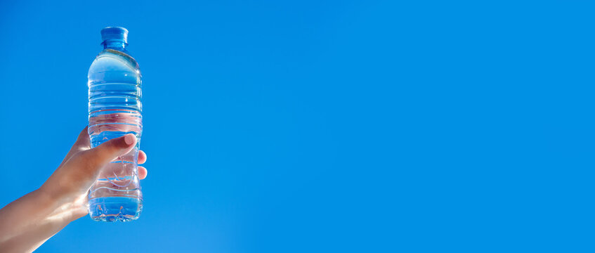 A girl holds a bottle of drinking water in her hand against a blue sky background