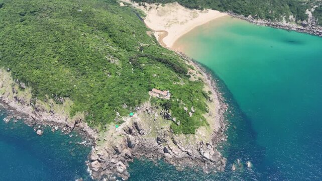 Drone footage captured orbiting Mui Dien Lighthouse and Bai Mon Beach in Dak Lak (formerly Phu Yen) Province, Vietnam. The aerial view reveals the iconic lighthouse, crescent-shaped sandy beach, and s