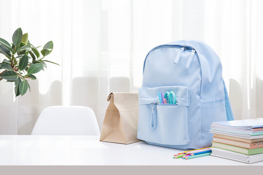 Workspace with school supplies and blue backpack near curtained window in sunlight