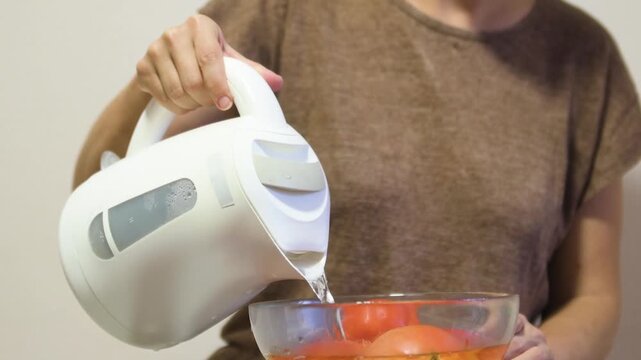 Woman Pouring Boiling Water from Kettle to Blanch Tomatoes in Glass Bowl for Peeling
