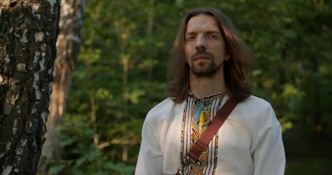 Caucasian man with long hair and Ukrainian traditional folk attire walk wandering on nature. 4K 10-bit