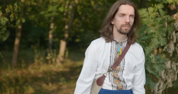 Caucasian man with long hair and Ukrainian traditional folk attire walk wandering on nature. 4K 10-bit