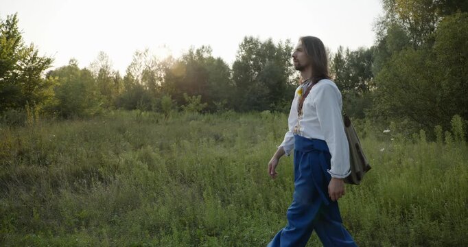 Caucasian man with long hair and Ukrainian traditional folk attire walk wandering on nature. 4K 10-bit