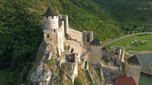 Aerial around view of Golubac medieval fortress on cliff above Danube river at sunset, historic landmark in Serbia, 4k