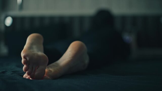 women's feet resting in a dimly lit room with string lights and a dark surface, creating a relaxed atmosphere in a cozy indoor setting with textile and wooden floor elements.