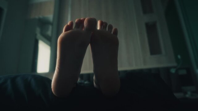 women's bare feet soles lifted above bedding with gentle toe flex and relaxed reclining pose in moody bedroom interior, soft daylight, muted tones, intimate calm scene