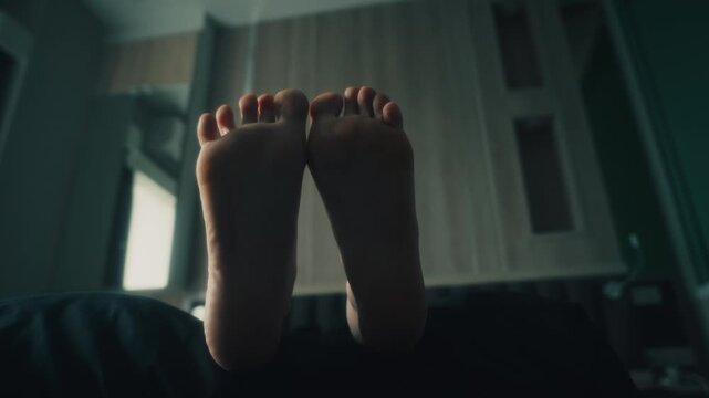 women's bare feet soles lifted above bedding with gentle toe flex and relaxed reclining pose in moody bedroom interior, soft daylight, muted tones, intimate calm scene