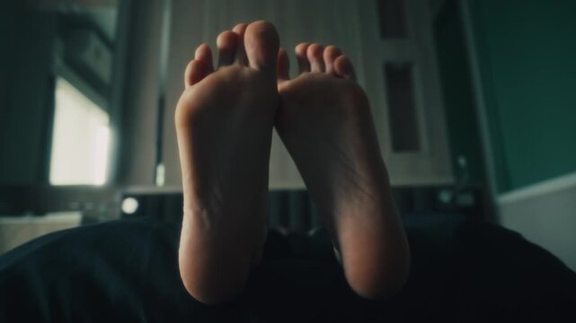 women's bare feet soles lifted above bedding with gentle toe flex and relaxed reclining pose in moody bedroom interior, soft daylight, muted tones, intimate calm scene