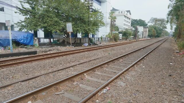 Parallel railway tracks running through a suburban area with green trees and buildings.